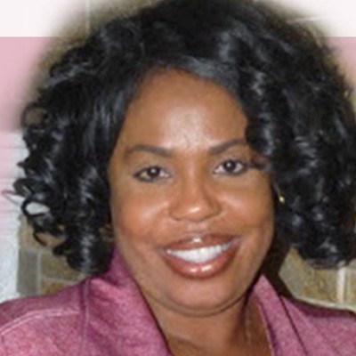 Portrait of a smiling woman with curly dark hair and a pink jacket. 